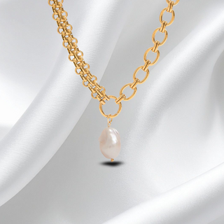 Gold chain necklace with a pearl pendant on a white fabric background