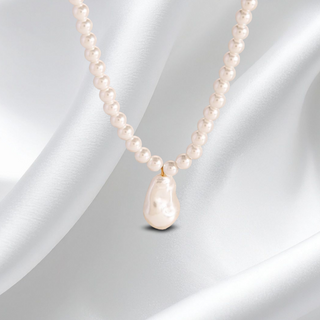 Pearl necklace with a teardrop-shaped pearl pendant on a white fabric background