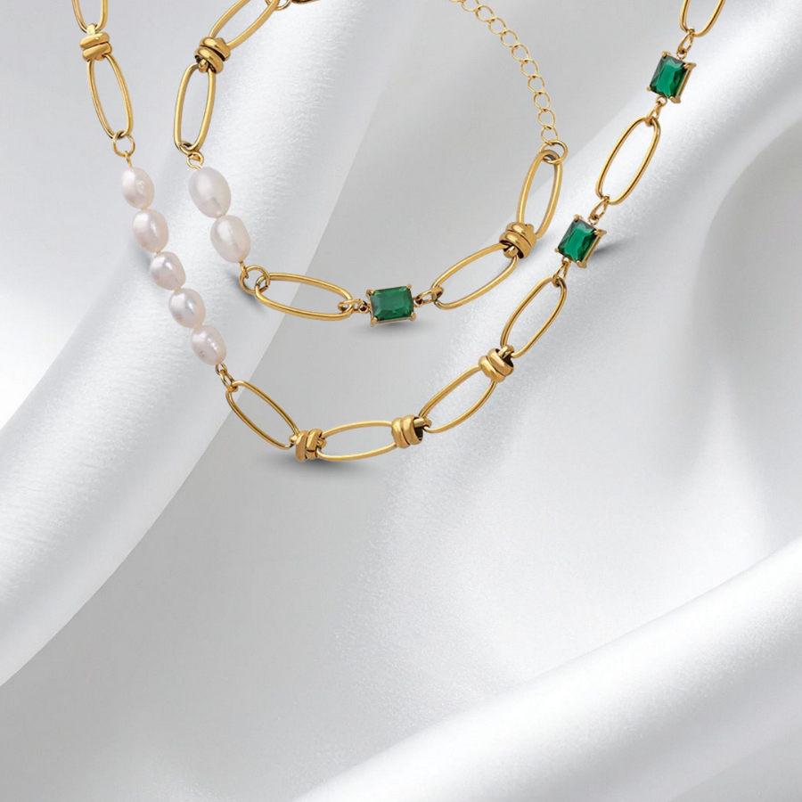 Gold necklace with green and white beads on a white fabric background