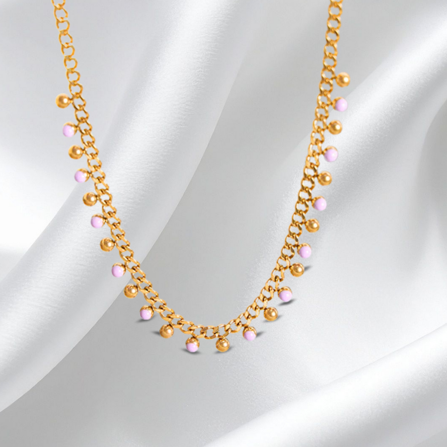 Gold necklace with pink beads on a white fabric background