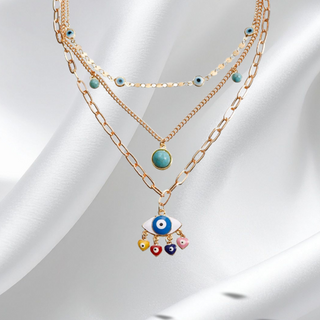 Layered gold chain necklace with colorful evil eye pendant on a white fabric background