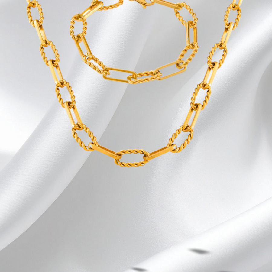 Gold chain necklace and bracelet on a white fabric background