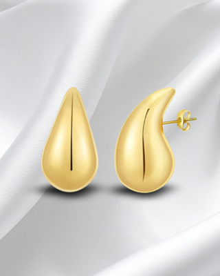 Gold teardrop-shaped earrings on a white fabric background