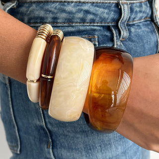 Close-up of a person's wrist wearing three amber-colored bangles with gold accents.