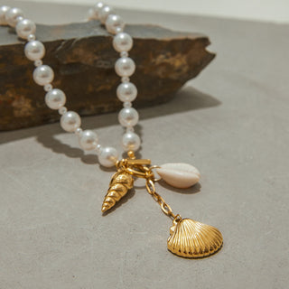 Pearl necklace with gold shell charms on a textured surface