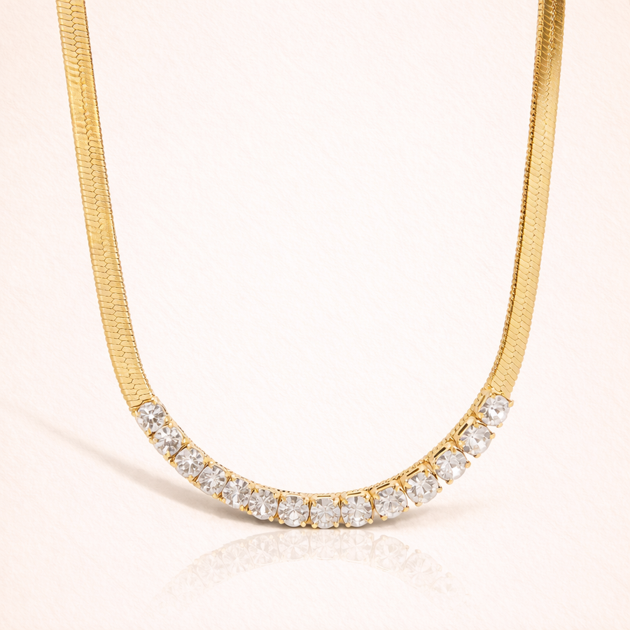 Gold necklace with clear stones on a light pink background