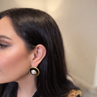 woman wearing a black and gold earring with a pearl center.