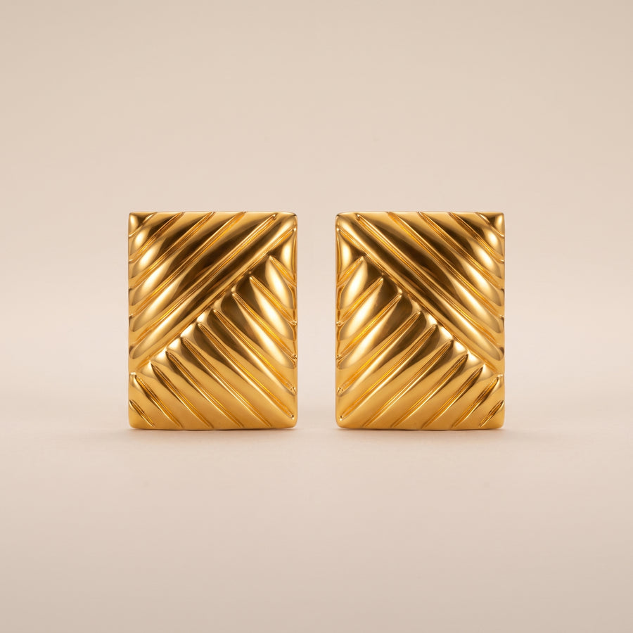 A pair of gold square cufflinks with a textured diagonal chevron pattern, displayed on a neutral beige background.