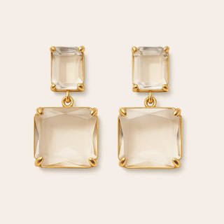 smoddo Gold earrings with clear gemstones on a beige background