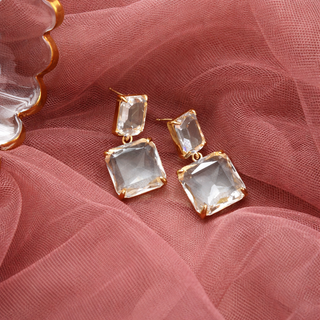 Gold earrings with clear gemstones on a pink fabric background