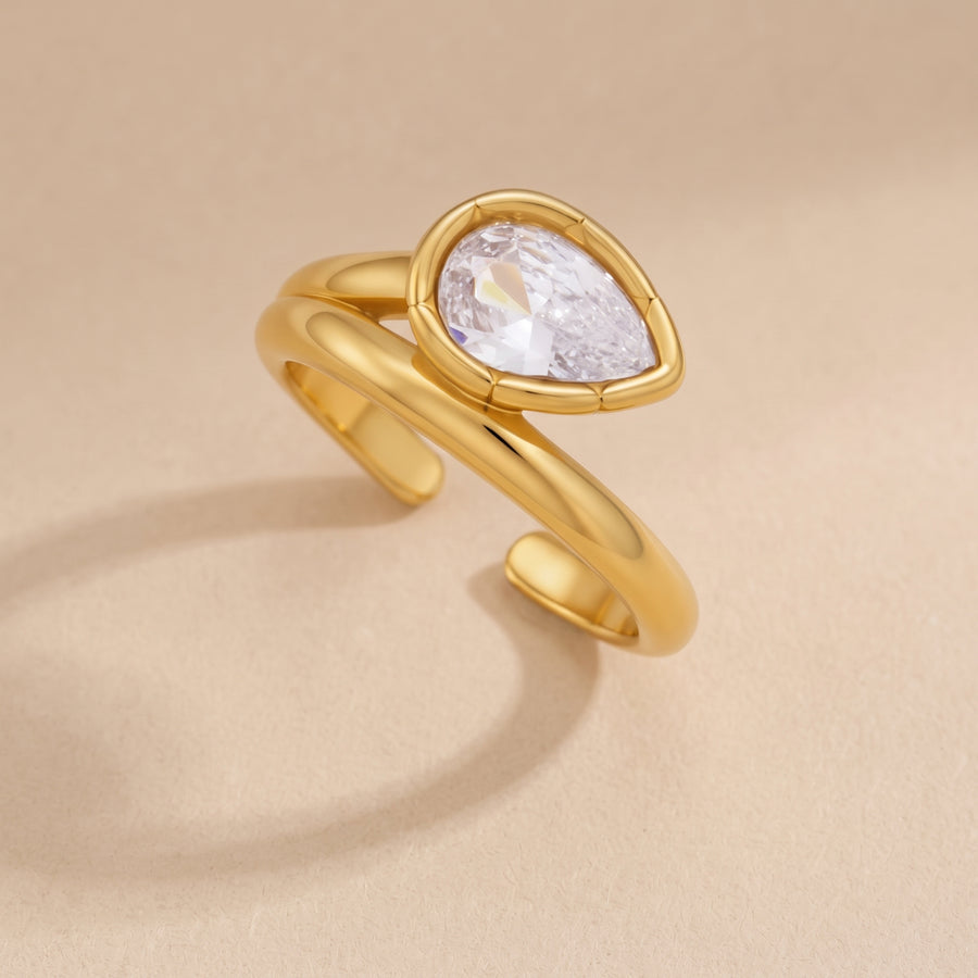 Bezel Elongated Ring in 18K gold with a bezel-set pear-cut clear zircon, close-up on a neutral beige background