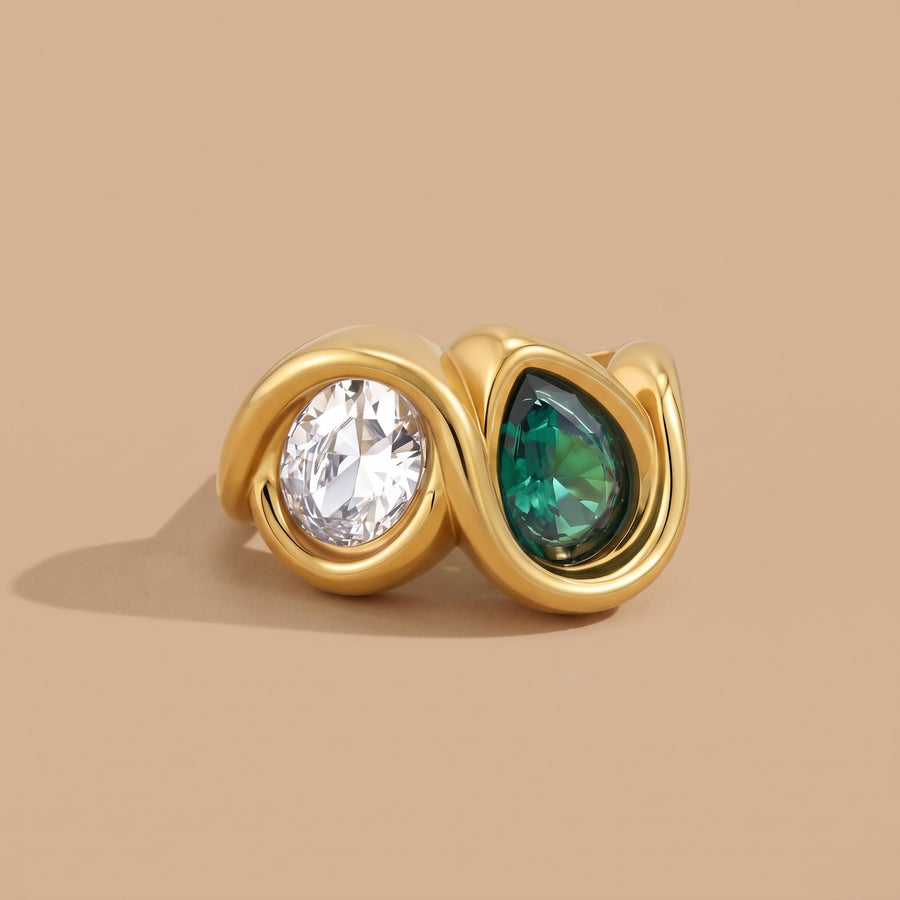 Bezel Emerald Ring in 18K gold with bezel-set clear and emerald zircon stones, close-up on a beige background