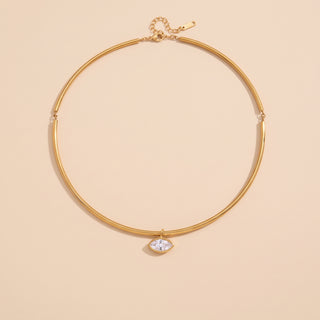 A gold-toned bangle-style necklace with a small marquise-cut clear gemstone pendant, displayed on a solid pale peach background.