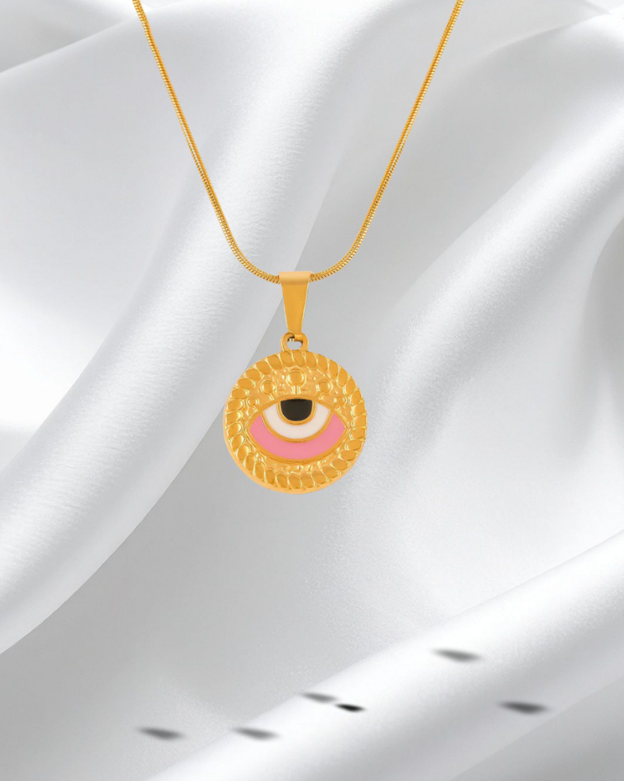 Gold necklace with a round pendant featuring an eye design on a white fabric background