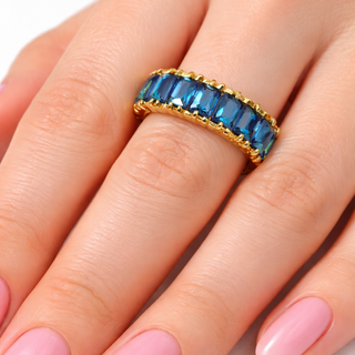 Gold ring with blue gemstones on a hand with pink nail polish