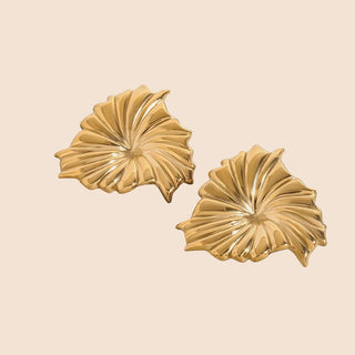 Pair of gold leaf-shaped earrings on a gray background
