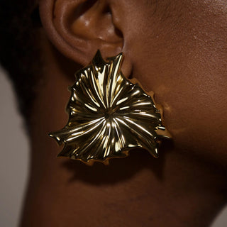 Gold leaf-shaped earring worn on an ear with a neutral background