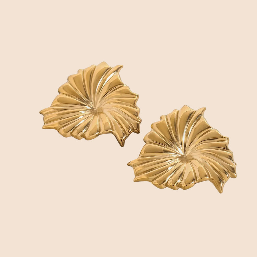 Pair of gold leaf-shaped earrings on a gray background