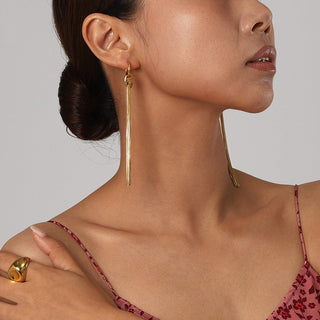 Woman wearing gold earrings and a ring with a plain background