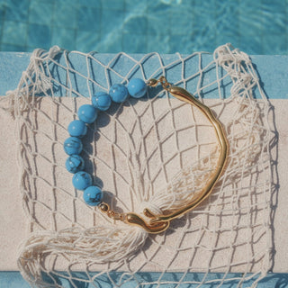 Bracelet with blue beads and gold clasp on a textured surface near a pool.