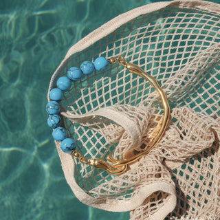 Bracelet with blue beads and gold clasp on a textured surface with water in the background