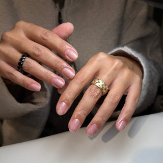 Close-up of hands with pink nail polish and gold rings on a neutral background
