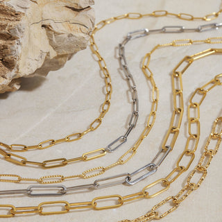 Gold and silver chain necklaces on a textured beige surface