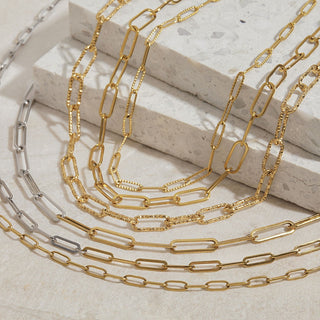 Gold and silver chain necklaces on a light stone surface textured paperclip