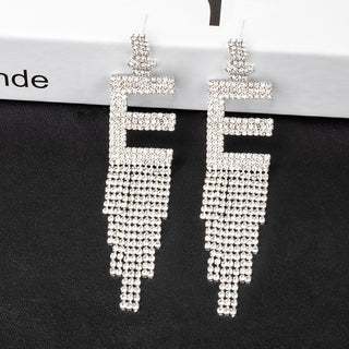 smoddo letter tassel Silver beaded earrings on a black stand with a blurred background