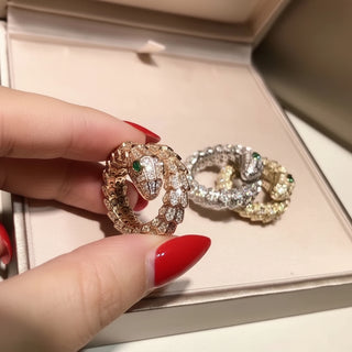 SMODDO adjustable snake ring in  Gold silver and rose gold snake-shaped rings with gemstones held by a hand with red nail polish on a light pink background.