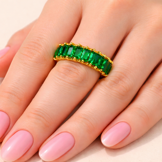 Gold ring with green gemstones on a hand with pink nail polish