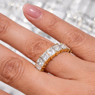 Close-up of a hand wearing two gold rings with diamond accents on a blurred background.