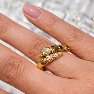 Gold  snake rings with diamond accents on a hand against a blurred glittery background