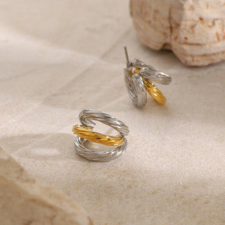 Pair of silver and gold spiral earrings on a textured beige surface with seashells.